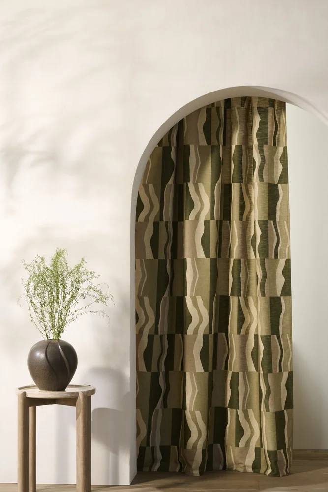 Curtains 13 Isara made-to-measure curtain in a green geometric wave pattern hung in an arched doorway, styled with a stone vase and dried grasses - Melksham Blind